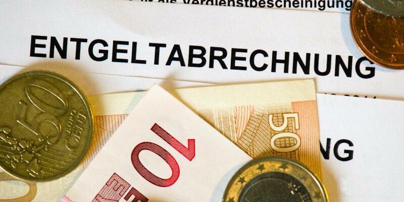 Eine Lohnabrechnung mit Geldmünzen und -scheinen - Foto: Arno Burgi/dpa-Zentralbild/dpa/Illustration